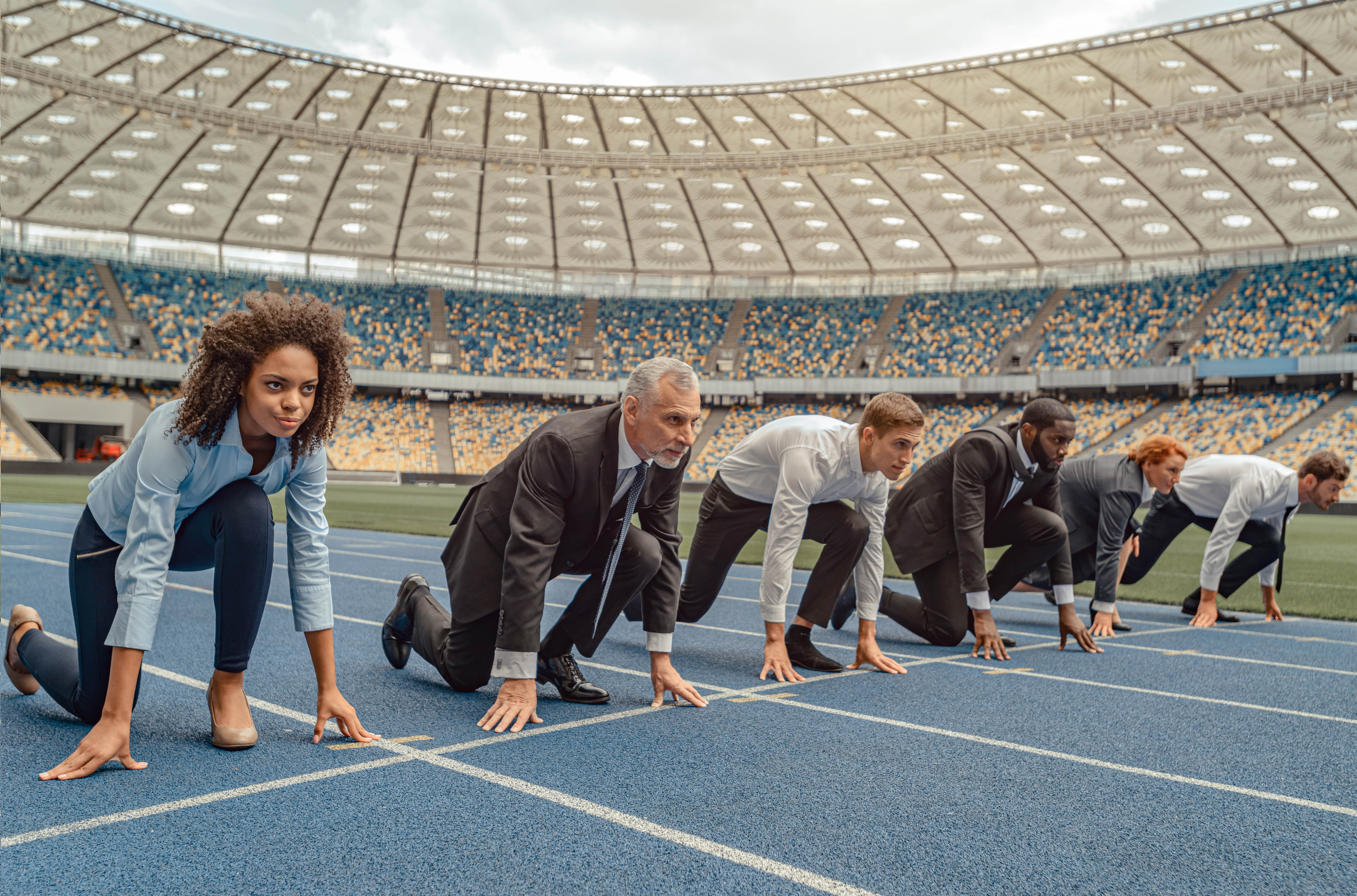 Businessmen and women standing at the starting line on a race track in a stadium